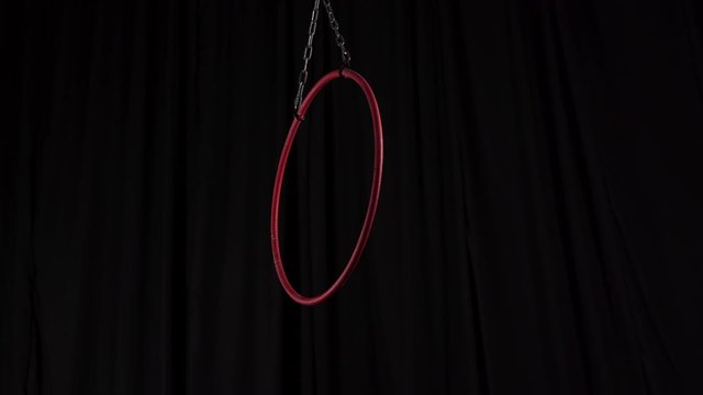 Video of metal red aerial ring for aerial gymnastics with metal chains attached to aerial hoop swinging to sides, circus props, equipment on black background, backstage, coulisse in 4K