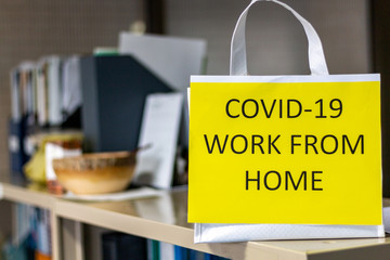 Secretary places a yellow sign Work from Home on the top of office cabinet. Workers work remotely during Coronavirus outbreak. Employee keeps social distancing to prevent 2019-nCoV contagious