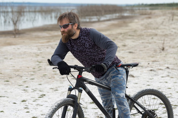 Fototapeta premium Sports brutal bearded guy on a modern mountain bike. A cyclist in a salt deserted place by the lake.
