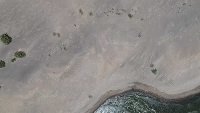 Top-down video of Lake Turkana greywater and waves lapping waves on a grey sandy beach 