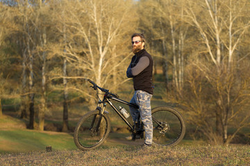 Obraz premium Sports brutal bearded guy on a modern mountain bike. Cyclist on the green hills in the spring.