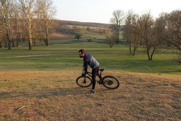 Cyclist in shorts and jersey on a modern carbon hardtail bike with an air suspension fork standing on a cliff against the background of fresh green spring forest