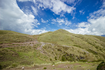 green field over mountains, blue sky and clouds