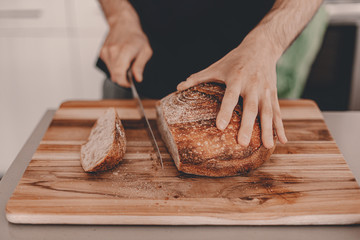 Homemade sourdough bread. Wheat rye flour. Man cuts the bread on cutting board. Handcrafted. Food trends. Wooden cutting board. Men's hands. Horizontal landscape image. Stay home, cook bread.