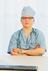 A female doctor is sitting at a table with a stethoscope on top of a suit.