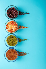 Glass jars with cereal mung bean, lentils, beans, brown rice on a blue background.