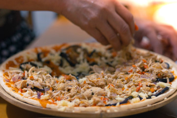 A person hand adding ingredients to  a traditional Italian Pizza with tomato sauce, cheese and sausage on wooden table background, front view. Grandmother's recipe. Homemade