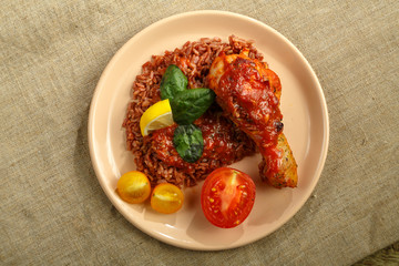 Chicken legs with red rice in tomato-garlic sauce on a plate top view.