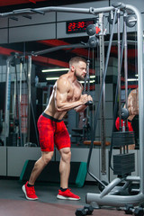 Fototapeta premium Strong muscular man is training his triceps using sport equipment in the modern gym