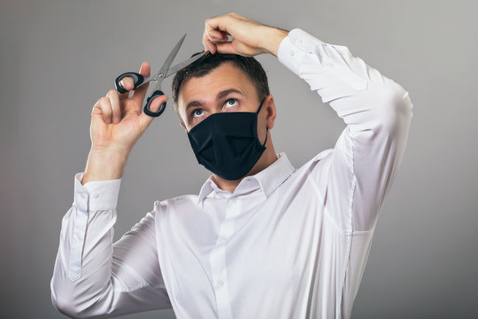 A man in a medical mask is trying to independently provide himself with hairdressing services while at home quarantine. Concept on the topic of closed beauty salons because of the pandemic covid-19