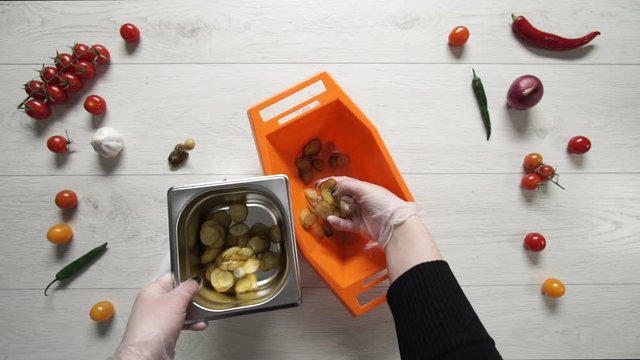 Chief takes slice of pickle cucumbers from plastic bowl and puts them to metal container