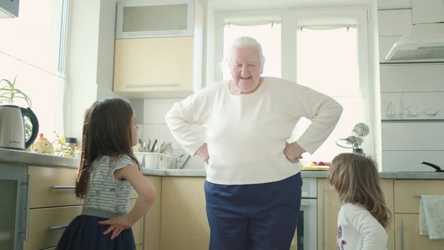 Old Grandmother Dancing In The Kitchen With Two Little Great-Grandchildren.