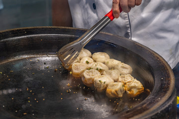 The chef using tongs while cooking Chinese fried dumplings 
