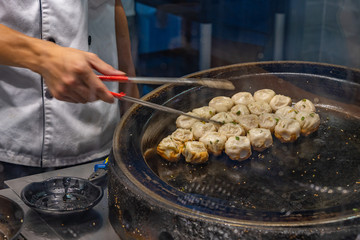 Chinese chef cooking fried dumplings on hot pan in kitchen