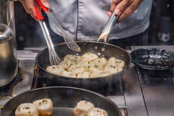 Chef's hands cooking Chinese fried dumplings on skillet 