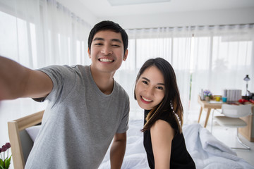 Asian couple lovers lying on their play mobile phones and selfie on bed  at home