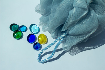 Fototapeta premium Blue mesh bath sponge abstract on white background with decorative blue and green glass beads, with copy space