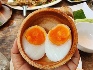 Asian woman holding a wooden cup with half boiled eggs inside Boiled duck egg and egg yolk, beautiful color, appetizing in a brown cup Top view from inside the restaurant
