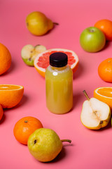 Fruit is scattered around the juice bottle on a pink background