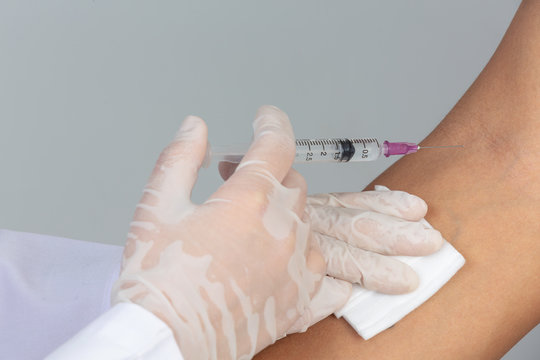 Young doctor is injecting the patient with  hypodermic syringe on gray background.