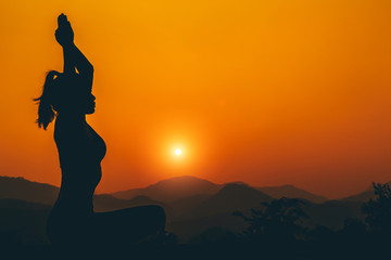 Silhouette - Yoga girl is practicing on the rooftop while sunset.