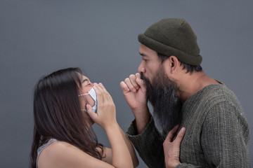 Old man is trying to coughing to young girl that is wearing mass while trying to covering mouth by hand on black background.