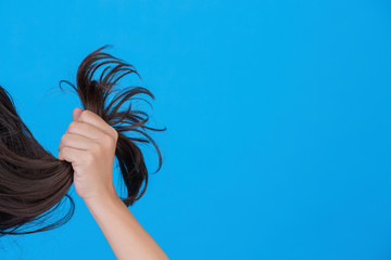 Black hair  young girl is pulling out of her hair on blue background, in studio.