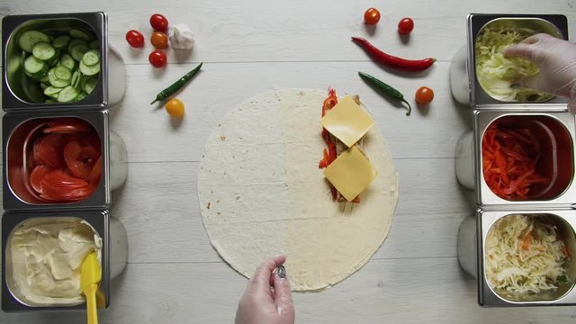 Top view of chef hands in white gloves puts cabbage on doner kebab shawarma in pita or lavash. Shawarma with chicken cutlet, pappers, cheese and vegetable