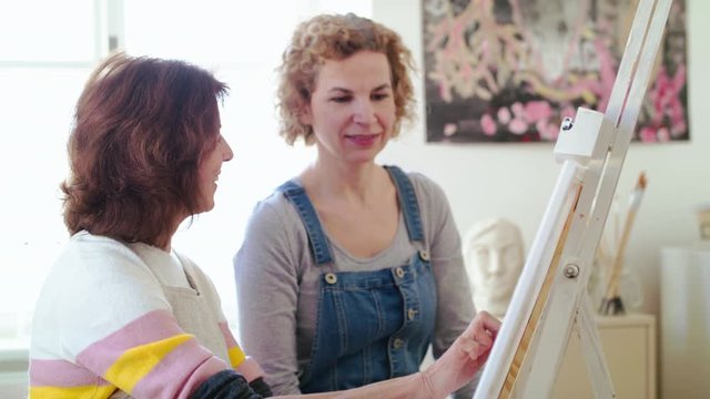 Senior woman with teacher painting pictures in art class.