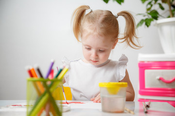 A Little Girl, With Tails On Her Head, Draws Watercolors Sitting At a Table. The Child Likes To Be Creative