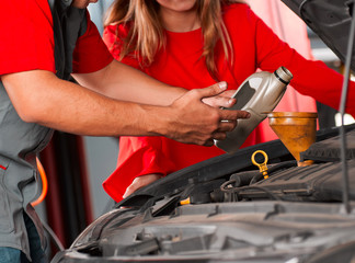 Photo of a mechanic technician changing oil, tuning vehicle, with customer watching and explaining...