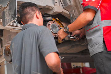 Close up photo of two mechanics working together, replacing rear drum brakes on a pickup truck  in...