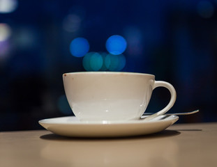 White ceramic coffee cup and saucer on a table with defocused blue lights in the background at a caf&eacute; in Kathmandu, Nepal