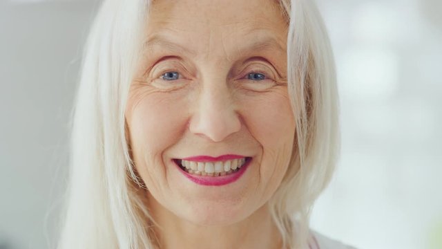 Authentic Beauty Portrait Footage of Senior Female Pensioner in a Bright Room at Home. Beautiful Old Female with Gray Hair Poses for the Camera and Gently Smiles. Happy Elderly Person Full of Health.