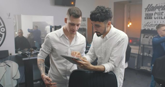 Barbers with digital tablet talking and standing in salon.