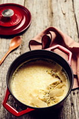 Creamy Polenta with baked onion and cheese in cast iron pot on rustic wooden background. Italian food. Selective focus. Toned image