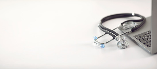 Doctor online. A stethoscope is on a white table with a laptop in blur at the hospital office.