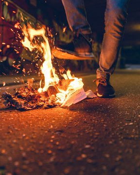 Low Section Of Man Standing By Burning Papers On Street At Night