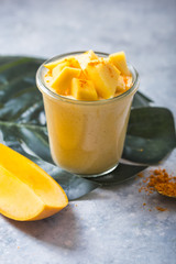 Yellow mango yogurt or smoothie on grey background. Turmeric Lassie or lassi in glass.