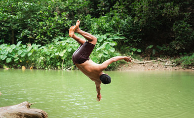 A young Asian man is jumping on a stream.