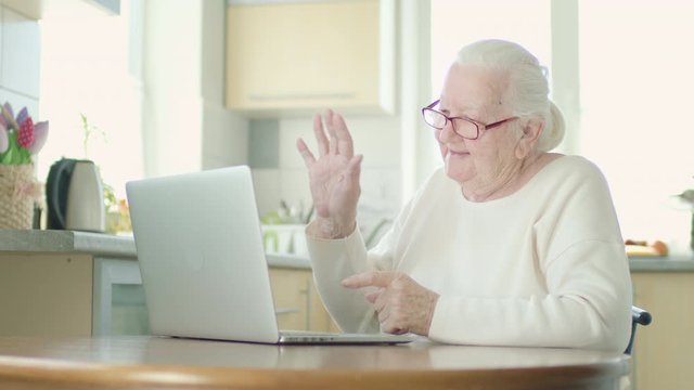 Gray-Haired Grandmother In Glasses Looks Intently At The Laptop Screen. Woman Talking To Someone Over Video Call.