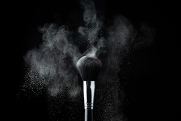 Make-up brush with natural color powder splashes explosion on black background. Beauty concept.