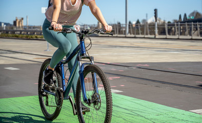 Girl in leggings rides a bicycle with a backpack behind her while riding a green bike path at the Tilikum Crossing Bridge in Portland