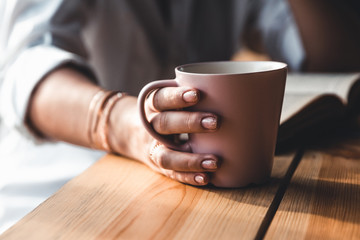 Woman in the morning drinks coffee and reads old book in a white shirt. Education, drink. manicure
