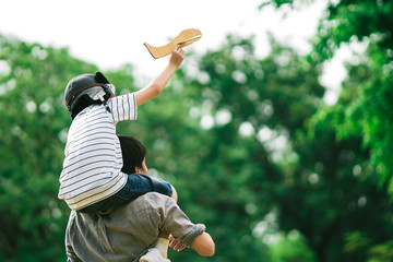 Father and son on his shoulder playing paper plane, spending time together at fresh green park in afternoon sunlight, the concept of family outdoor, daddy hero, Family background. Single Daddy and son