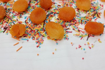 Decorative sprinkles border and dried apricots on white background. Multicolor Sugar confectionery powder and dried apricots in the corner. Scattered sweet sugar sticks and balls. Copy space.