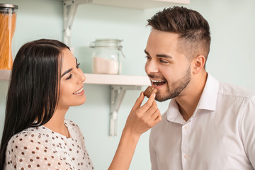 Beautiful young couple eating chocolate in kitchen