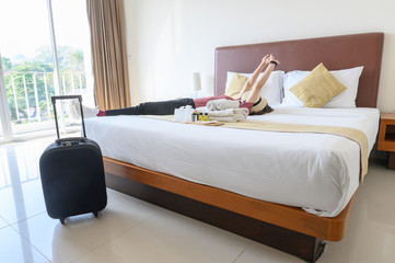 Portrait of tourist woman lying on the bed, stretching her hands with her luggage in hotel bedroom...