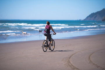 Fototapeta premium Woman in casual sportswear rides a bicycle along the Pacific Ocean inhaling the healing sea air