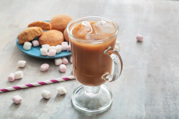 Glass cup of tasty iced coffee with sweets on grey background